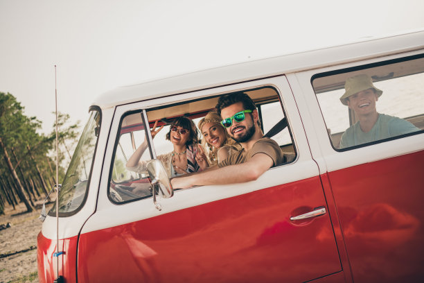 积极的嬉皮士朋友们在城市海边的面包车外侧面照片，向男士打招呼。图片下载