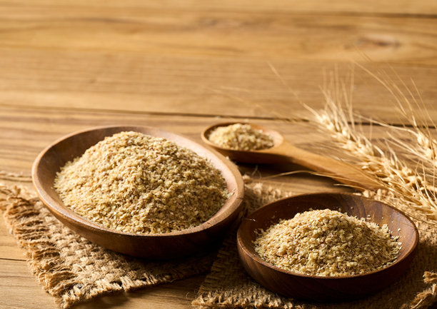 一堆全谷物粉或小麦胚芽放在木碗和木勺中，背景为木质桌面，具有乡村风格，留有空白空间。图片下载