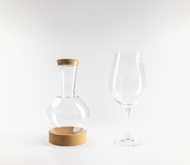 透明球形酒壶的模型，配有透明的软木塞和底座，以及玻璃酒杯，背景为白色，留有空白区域，真实照片图片下载