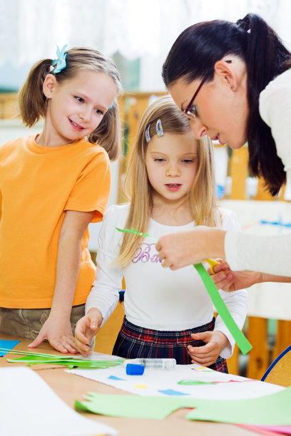 两个小女孩在看老师为拼贴画剪纸。图片下载