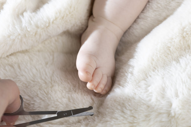 妈妈用婴儿剪刀修剪宝宝的指甲。特写照片显示母亲的手握着婴儿的脚和指甲剪。图片下载