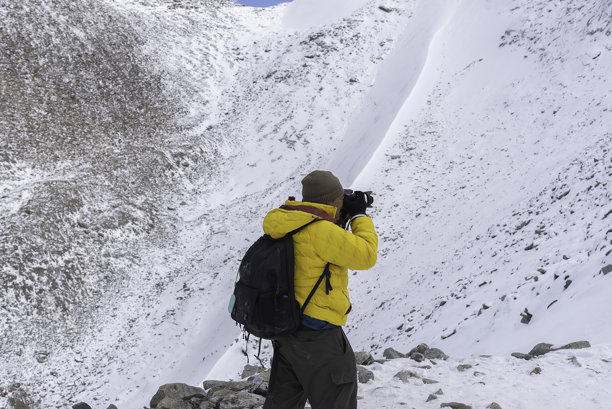 摄影师在雪山中背着背包进行徒步旅行拍摄冬季照片图片下载