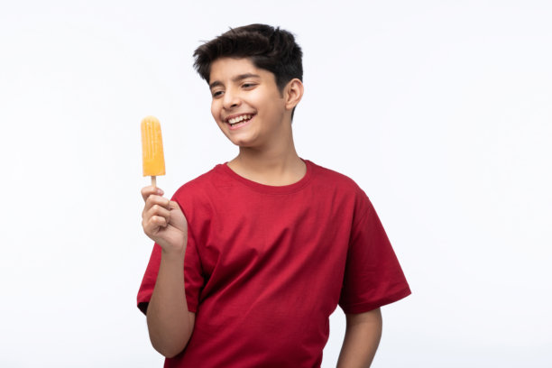 穿着红色T恤的少年男孩在白色背景下吃冰淇淋的肖像照片图片下载