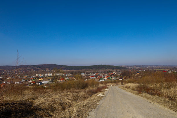 这张照片展示了一个位于山谷中小镇的全景。前景中可以看到一条从山上蜿蜒而下的土路，周围是干枯的草地和灌木丛。图片下载