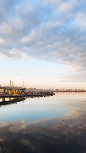春季风景。美丽的海湾晨曦全景。明亮的光线下，水面上漂浮着积云。海中有一只渔船。阳光的光芒映照在海岸线上。竖版照片图片下载