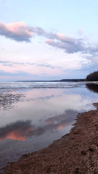 春季风景。美丽的黎明全景，海湾上方的积云在明亮的光线下。海岸线上有冰、雪和岩石。阳光的光芒在海面上反射。竖版照片图片下载