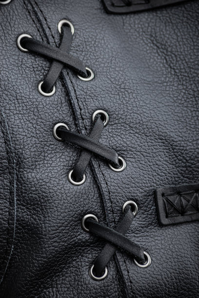 黑色皮革夹克的细节特写。这张图片展示了黑色无袖夹克侧面的装饰性系带细节。黑色鞋带穿过银色眼孔，形成交叉图案。图片下载