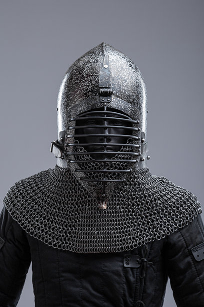 带有波纹面罩和链甲的黑暗头盔。这张图片展示了一顶深色，可能是黑色钢制的头盔，顶部尖锐，面罩上有一系列水平的波纹。头盔底部延伸出一条链甲领。图片下载