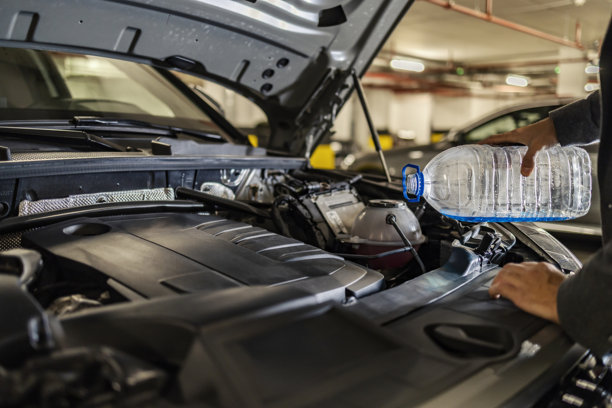在车库里，一个男人正在给汽车倒防冻液的裁剪照片。图片下载