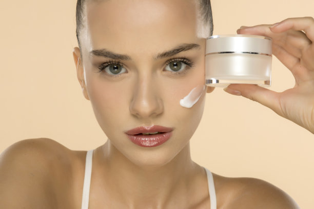 专业美容照片，女性展示护肤霜瓶，脸颊上有白色产品涂抹痕迹图片下载