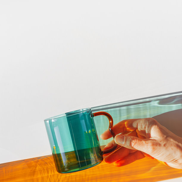 色彩斑斓的玻璃杯在明亮阳光下投射出阴影，透明的青色杯子在浅白色表面上投射出动态而生动的光线反射和阴影，创意美学的俯视图，简约照片图片下载