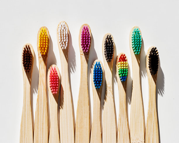 美观的米色竹牙刷，彩色刷毛在阳光下映衬于浅灰色背景。简约、卫生和环保的替代品，俯视照片，极简风格平铺。图片下载