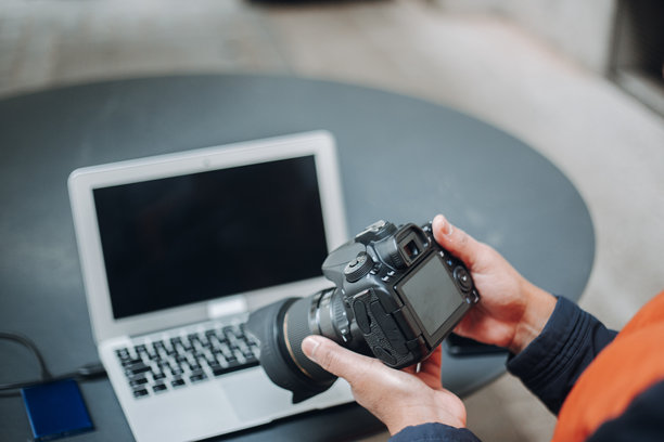 摄影师在拍摄后检查相机中的照片，桌上有笔记本电脑和硬盘。图片下载