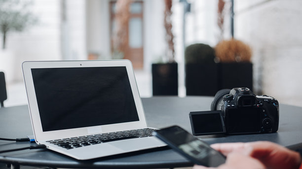 专业摄影师通过智能手机将相机照片同步到笔记本电脑，坐在配备尖端数字设备的极简桌子前。图片下载