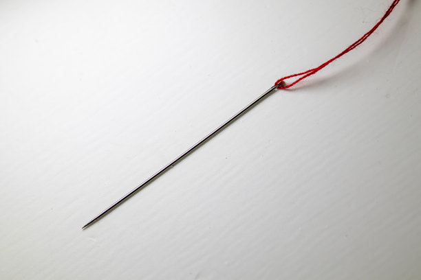 简约的微距照片，展示了一根白色背景上带有红色线的缝针。图片下载