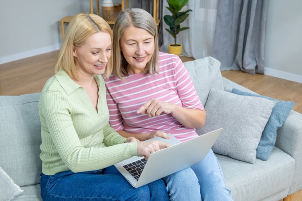 两位女性在笔记本电脑上查看旧照片，面带幸福和满足的笑容。图片下载