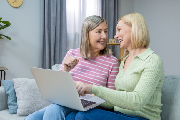 两位女性在笔记本电脑上查看旧照片，面带幸福和满足的笑容。图片下载