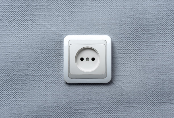 一个白色的欧式电墙插座安装在纹理细腻的浅灰色墙壁上。照片简约、居中且光线充足。图片下载