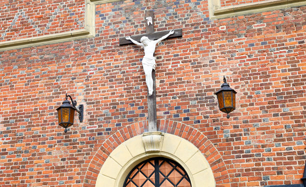 这张照片展示了耶稣基督的十字架刑，挂在教堂的墙上。十字架由白色材料制成，教堂的墙壁则是红砖结构。图片下载
