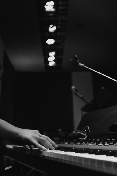 在舞台灯光下，一个人正在演奏电子键盘的特写。黑白照片捕捉了在昏暗场地中现场表演或排练时的音乐瞬间。图片下载