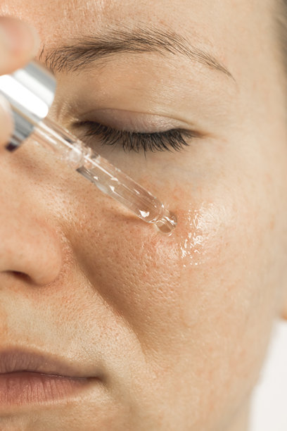 特写，垂直照片，一位女性在脸上涂抹保湿精华油。美容护理过程。图片下载