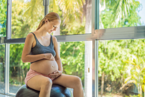 孕妇在家中使用健身球锻炼。孕妇正在用健身普拉提球进行放松练习。窗户作为背景。图片下载