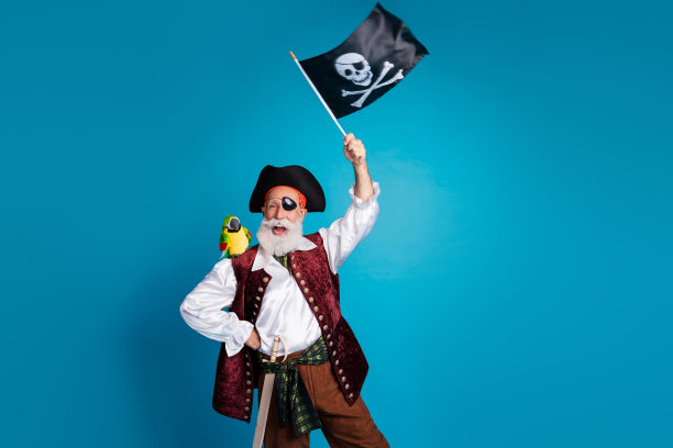 搞笑的老海盗爷爷在蓝色背景下挥舞着旗帜，穿着化妆舞会服装的照片肖像图片下载