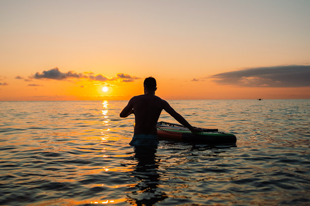 一名男子在海上日落时划着立式划水板。高质量照片图片下载
