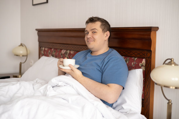 帅气的年轻男子在家中或酒店卧室的床上喝咖啡。早晨、舒适、食物和人们的概念。高质量照片。图片下载