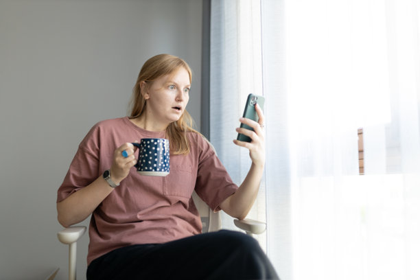 震惊、担忧的女孩在家中手持杯子并使用手机。高质量照片。负面情绪图片下载