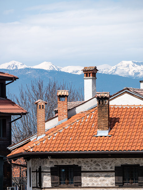 保加利亚班斯科的传统房屋在阳光明媚的早晨，背景是白雪皑皑的山脉 - 竖版照片图片下载
