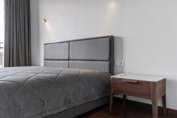 现代公寓的时尚卧室室内。灰色的大双人床配有干净的床单和灰色床罩。床旁边有时尚的木质床头柜。卧室的不同光线下的照片。图片下载