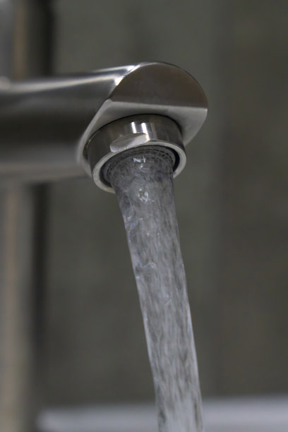 从拉丝镍水龙头流出的清水在浴室中营造出清新的氛围，强调卫生，促进空间的纯净感和健康感。竖版照片图片下载