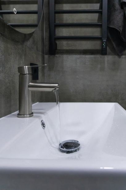 现代浴室水槽的特写，配有不锈钢水龙头、白色陶瓷盆和纹理混凝土墙，营造出时尚简约的氛围。竖版照片图片下载