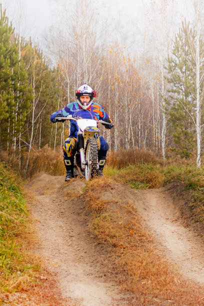 男子骑着越野摩托车穿越田野和森林。彩色设备，竖版照片图片下载