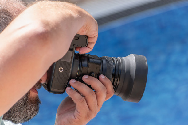 捕捉瞬间。留着胡子的摄影师手持相机，享受他的爱好，在阳光明媚的夏日泳池旁拍摄惊艳的照片。创造力、放松、对摄影的热情。图片下载