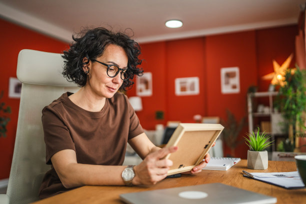成熟的女性在家工作时拿着并看着相框中的照片图片下载
