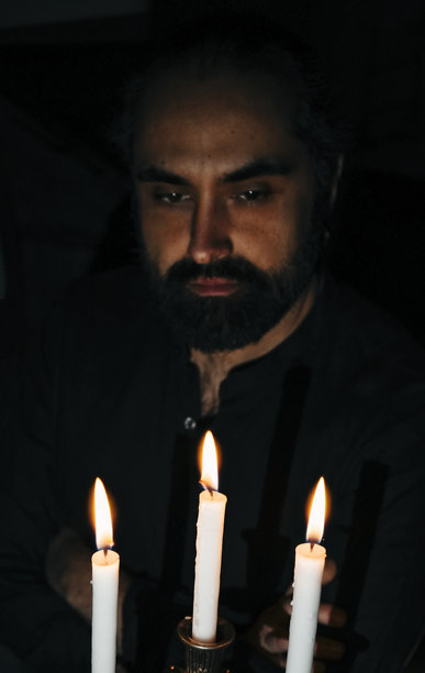 沉思的男人凝视着黑暗氛围中的蜡烛。竖版照片图片下载