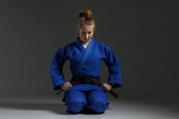 穿着白色道服、系着黑色腰带的女孩柔道选手，背景为蓝色，摄影棚照片图片下载