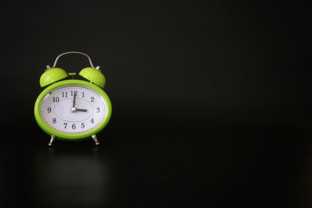 黑色背景上的绿色闹钟。时钟和时间主题的照片图片下载