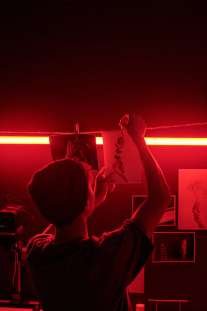 在暗房中，红光下，背影男子正在晾晒照片印刷品。图片下载