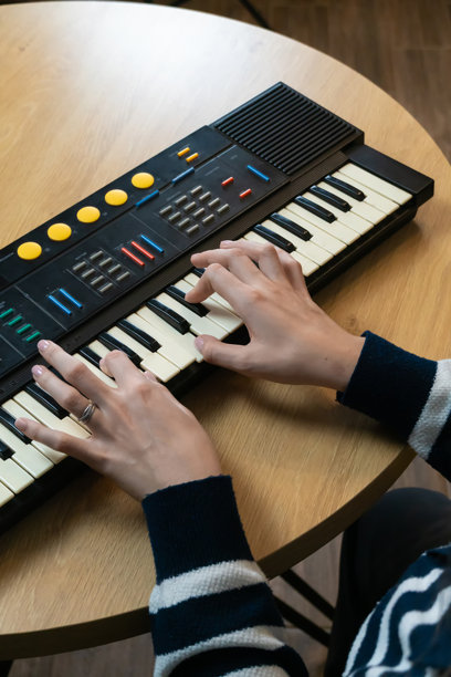 女性音乐家在木桌上演奏复古电子合成器键盘，创作音乐，展现创造力和热情，俯视角度拍摄。竖版照片图片下载