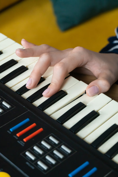 女性手部特写，正在演奏复古合成器键盘，在温馨的家居环境中创作电子音乐，背景有黄色沙发和绿色靠垫。竖版照片图片下载