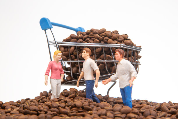 一张创意库存照片，展示了微型人物在咖啡豆上和装满咖啡豆的购物车，象征着咖啡贸易中的团队合作。图片下载