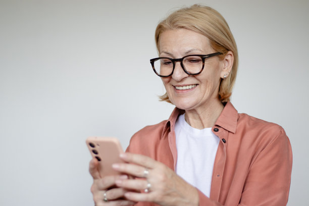 成熟的金发女性戴着眼镜，在白色背景前使用手机的工作室拍摄照片图片下载