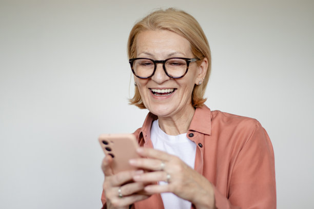 成熟的金发女性戴着眼镜，在白色背景前使用手机的工作室拍摄照片图片下载