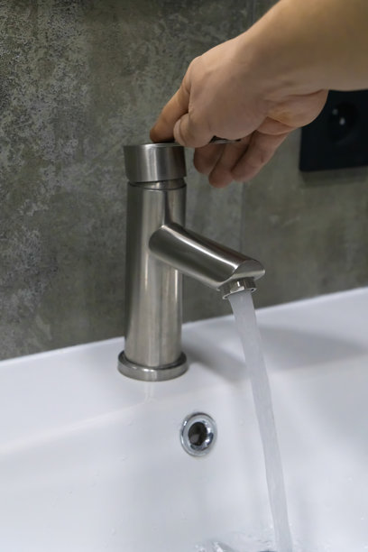 手在现代浴室的拉丝镍水龙头上转动，清澈的水流入干净的白色洗手盆，倡导节水和卫生。竖版照片图片下载
