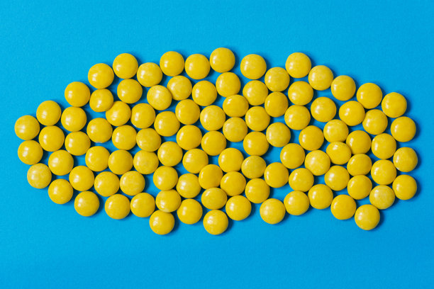 小巧的黄色巧克力涂层糖果，孤立在蓝色背景上，俯视或平铺照片。图片下载