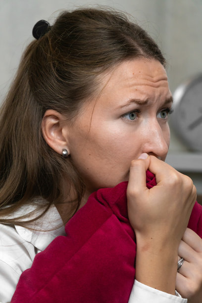 紧张的年轻女性紧握红色枕头，焦虑地咬着手指，周围弥漫着紧张的气氛，体现了职场中的担忧和情感压力。竖版照片图片下载