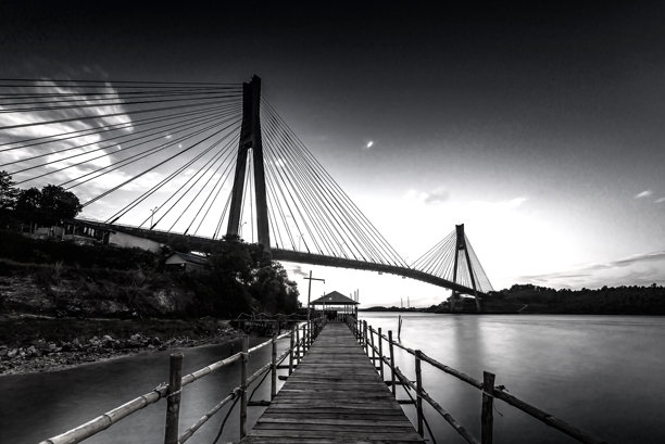 黑白照片，夕阳下的海上桥梁。图片下载